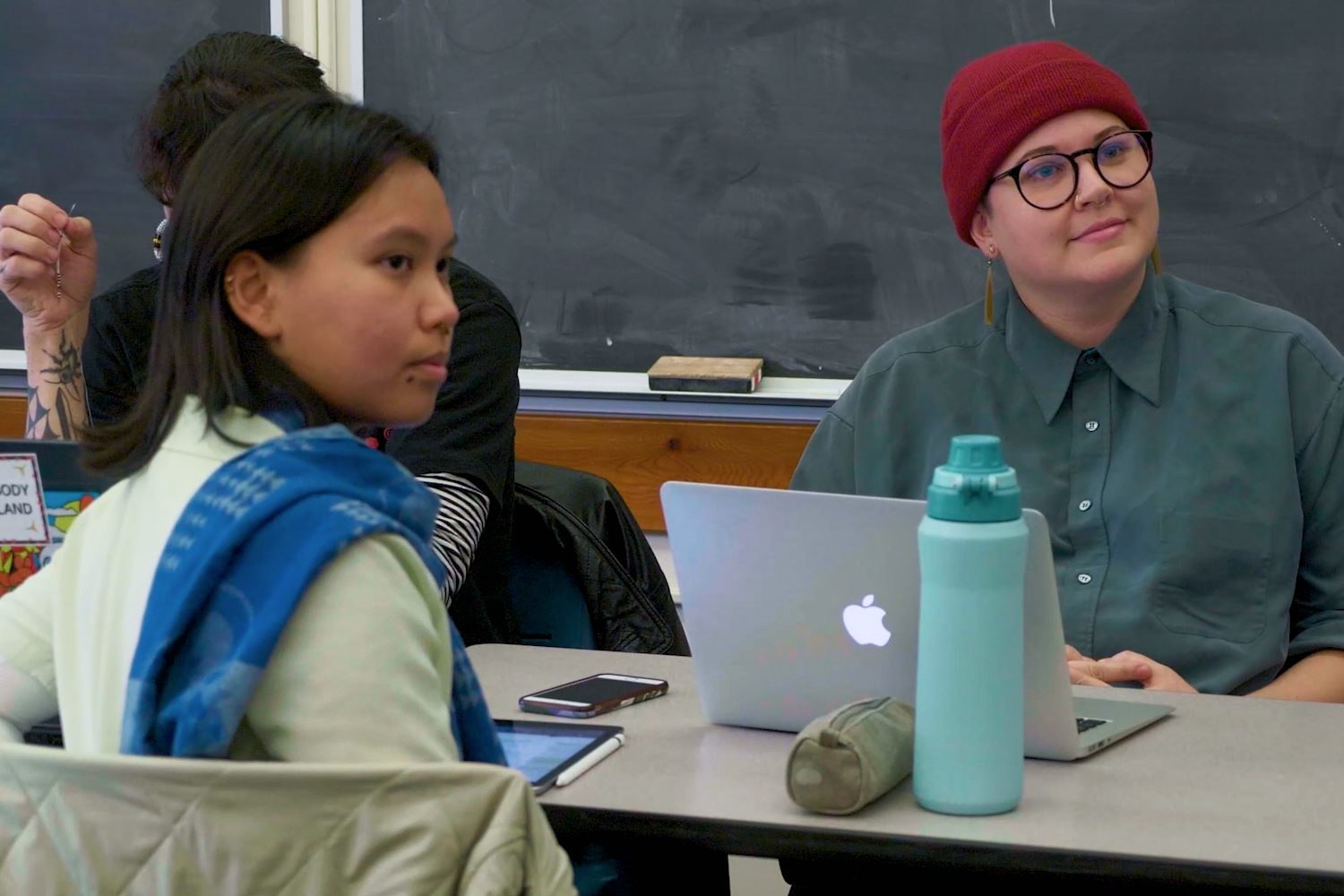 Two students in a classroom in front of a laptop and a tablet